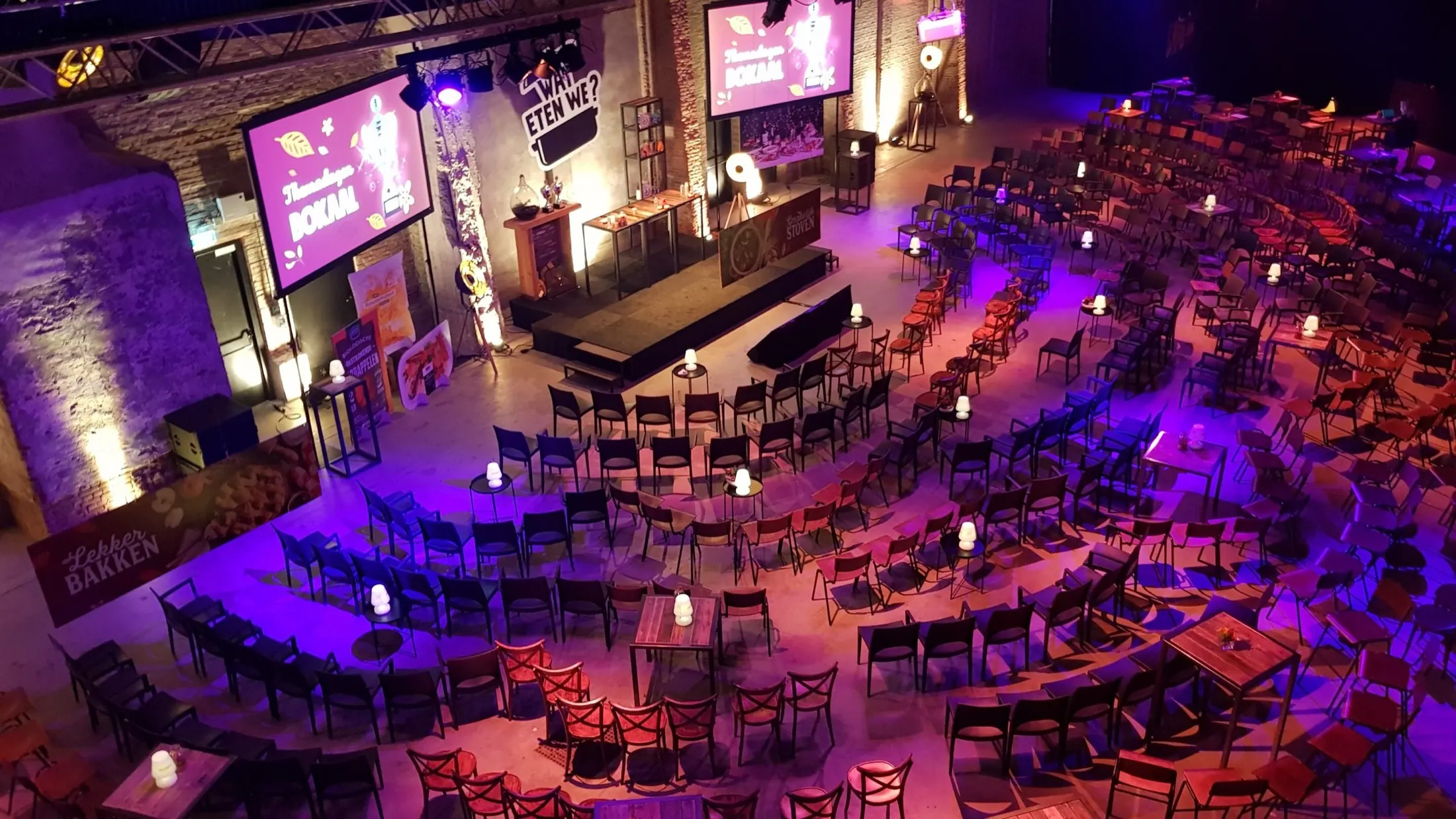 Industriële hal met theateropstelling, podium, schermen en paars licht