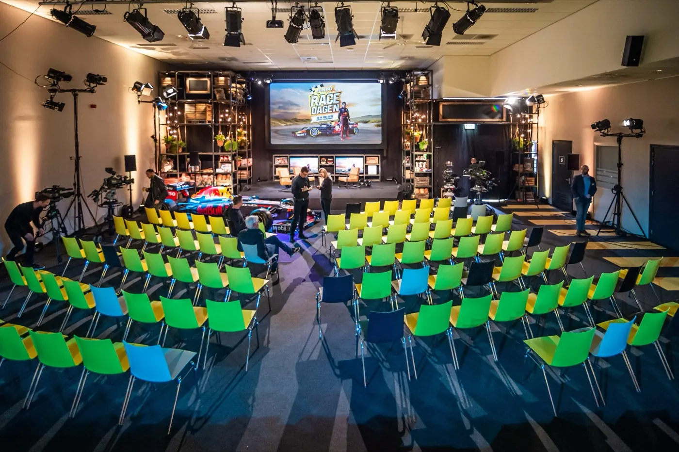 Zaal met groene stoelen, een raceauto en een groot scherm